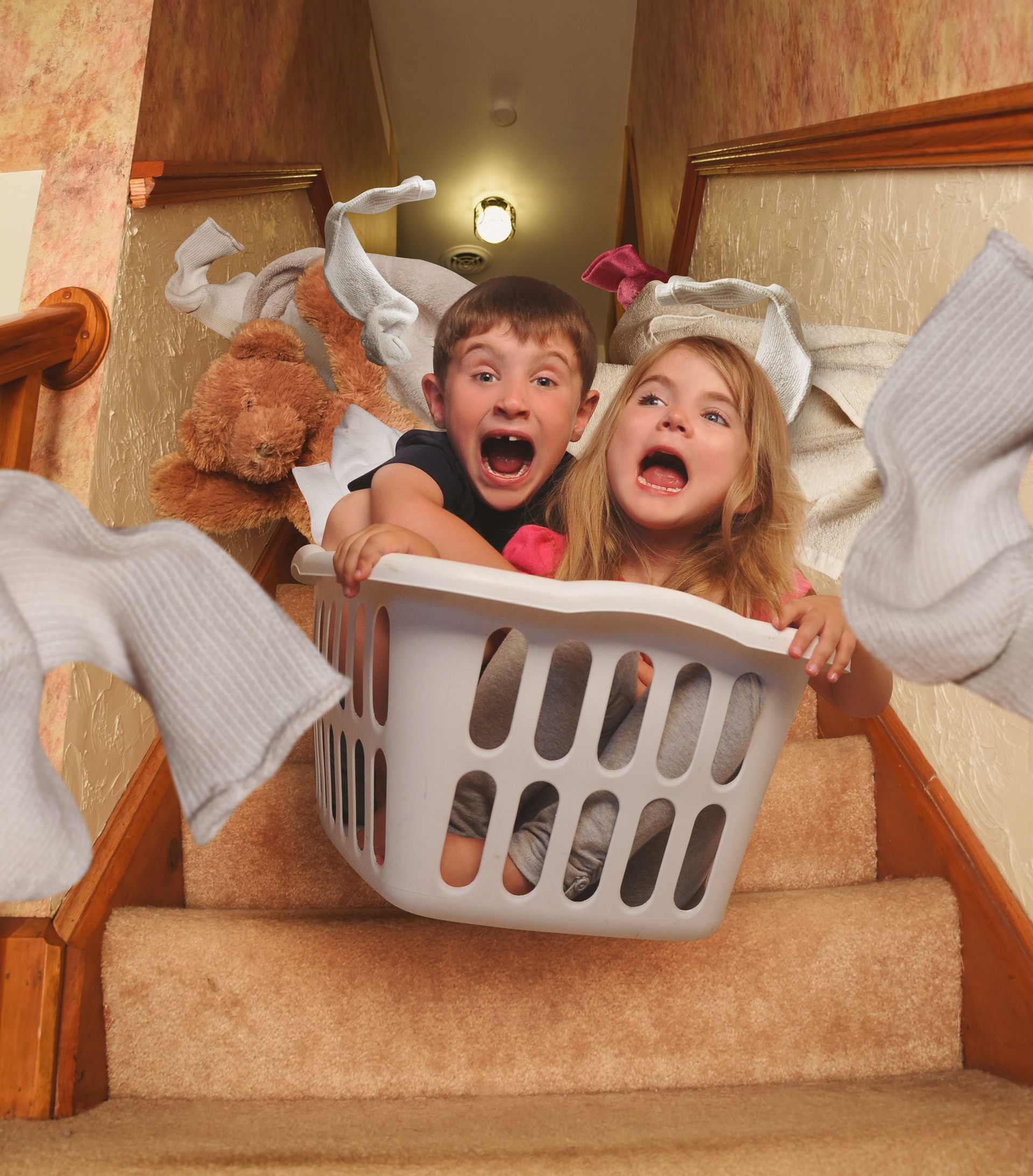 45151048 - two young children are riding in a laundrey basket down the house stairs with socks flying for a parenting, babysitter or humor concept.