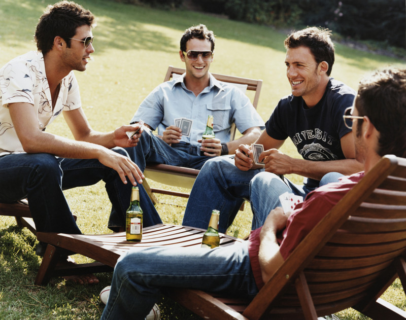 Group of Men Sitting on Sunloungers Playing Cards and Drinking Beer